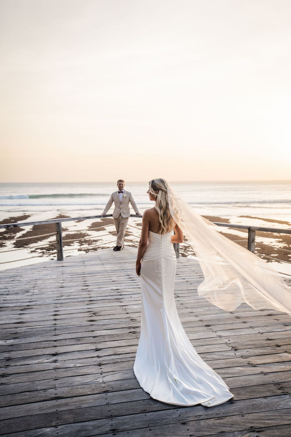 White wedding dress flowing in ocean breeze on wooden boardwalk at sunset.