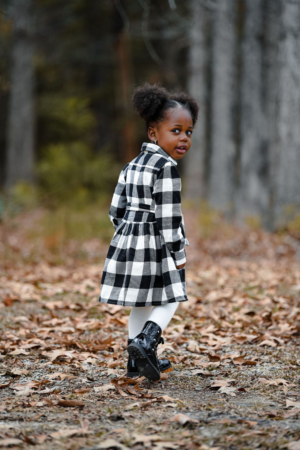 Child in black and white buffalo check dress walking through fallen leaves.