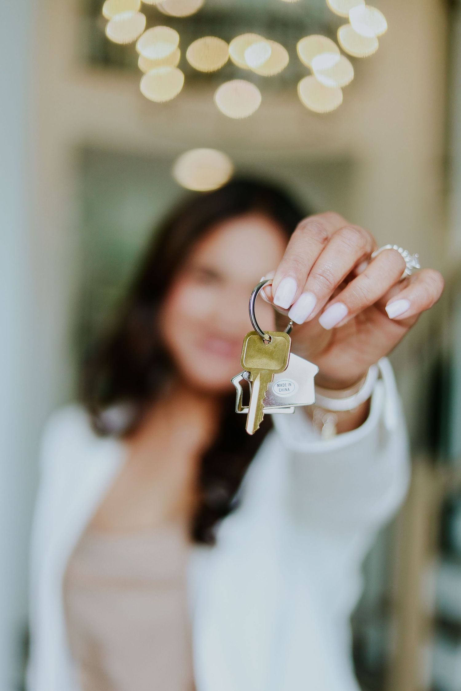 Close-up of hands holding house keys with bokeh lighting effects in background.