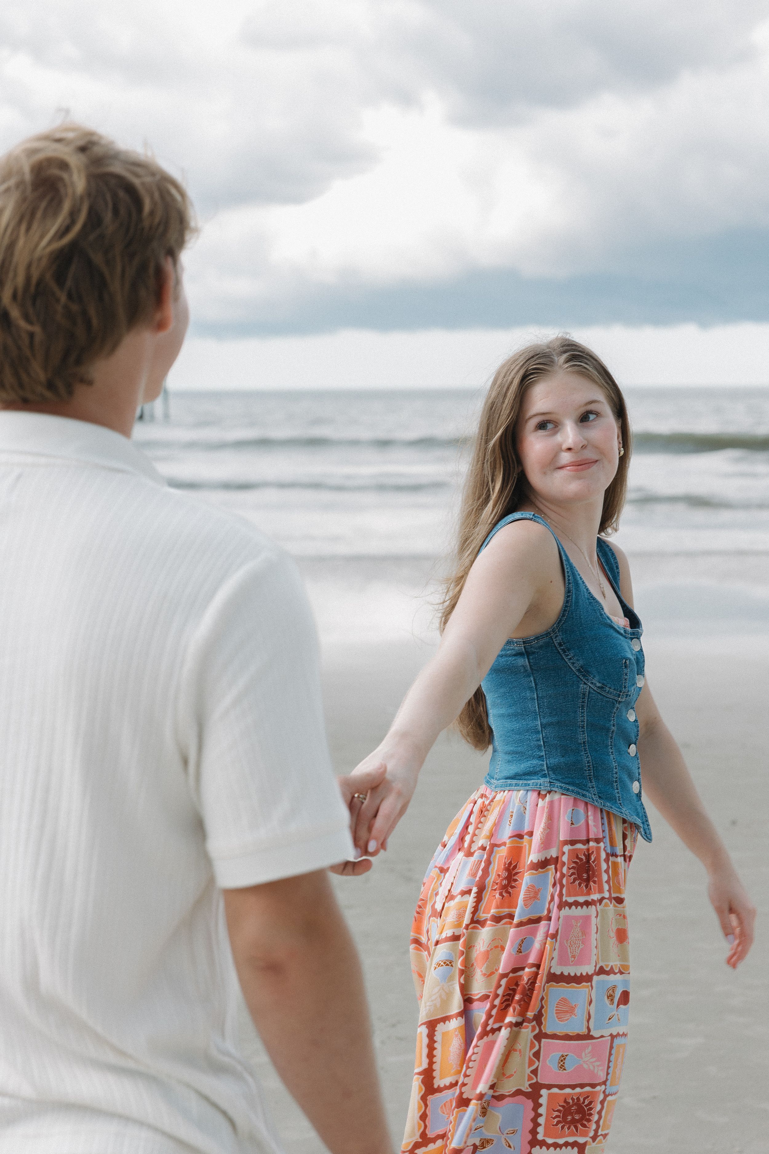 Couple walking together on a sunny beach with waves in the background.