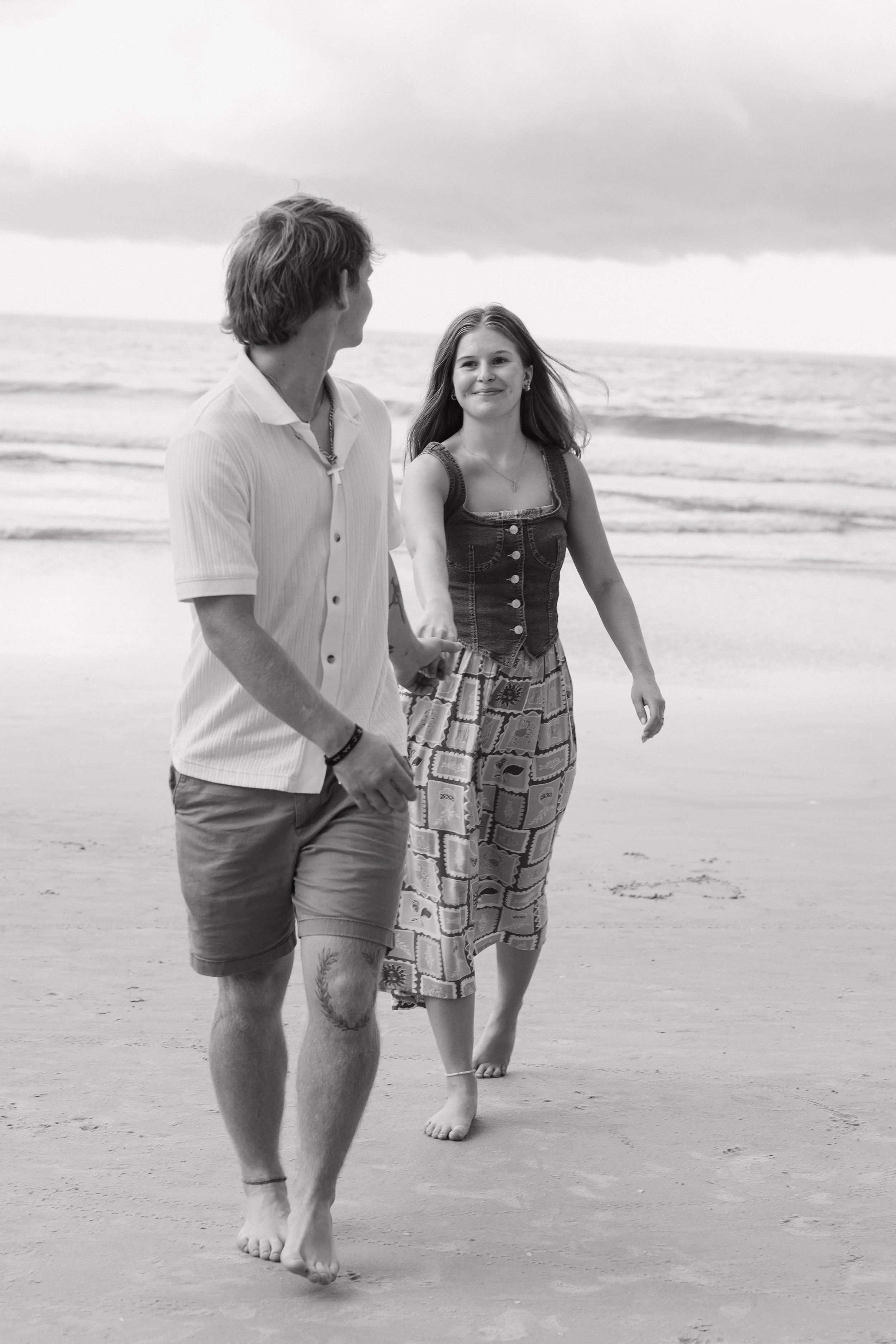 Couple strolling barefoot along the shoreline in casual summer attire.