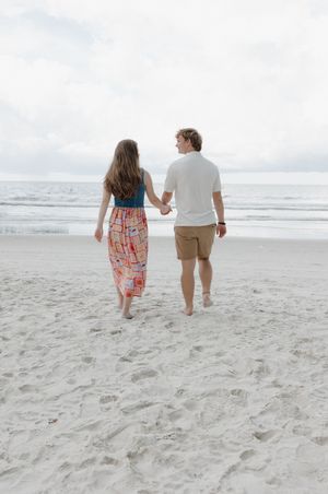 Couple walking away together on white sandy beach towards the ocean.