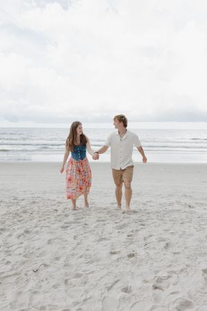 Couple playfully running and dancing together on a beach.