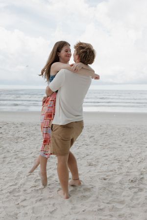 Couple embracing while standing in the sand with ocean waves behind them.