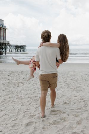 A playful sequence of a couple dancing and twirling together on a sandy beach near a pier.