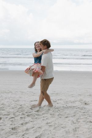 A couple shares a joyful dance sequence on the beach with ocean waves in the background.