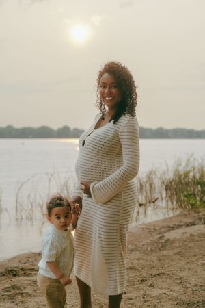 Family enjoying sunset at a lakeside beach with tall grass and sand in soft golden light.