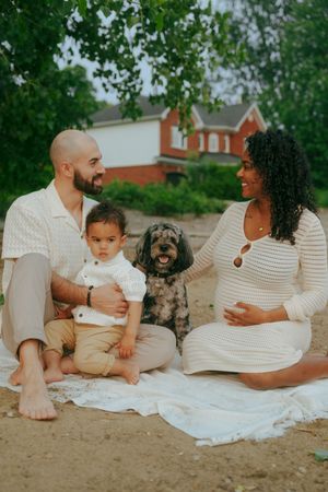 A family relaxes on a white blanket outdoors with their small dog while wearing coordinated light colored clothing.