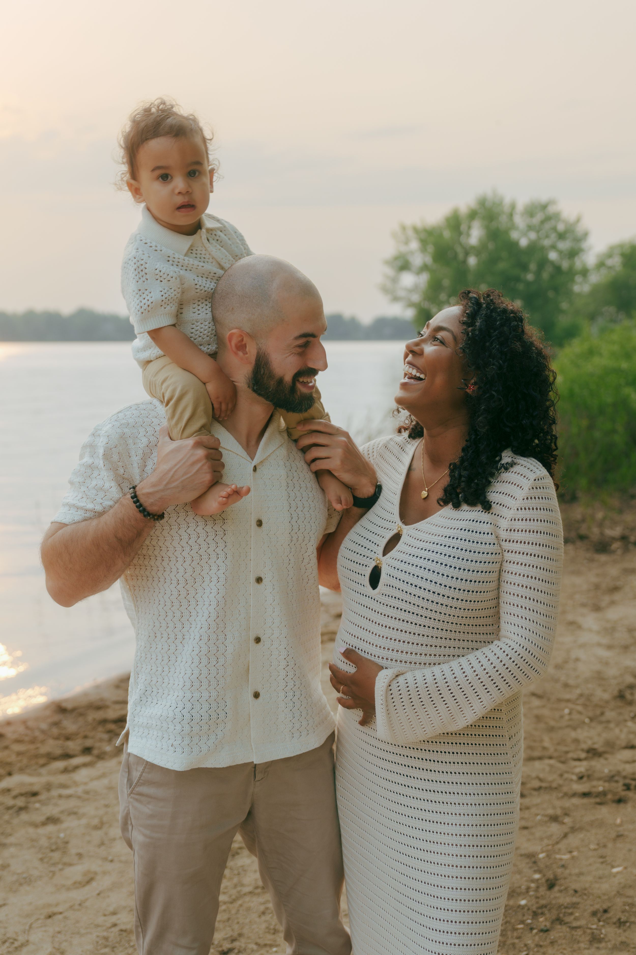 Family wearing coordinating white sweaters shares a joyful moment together on a beach at sunset.
