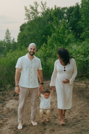 Family walking together on scenic woodland path wearing coordinated white and beige outfits.