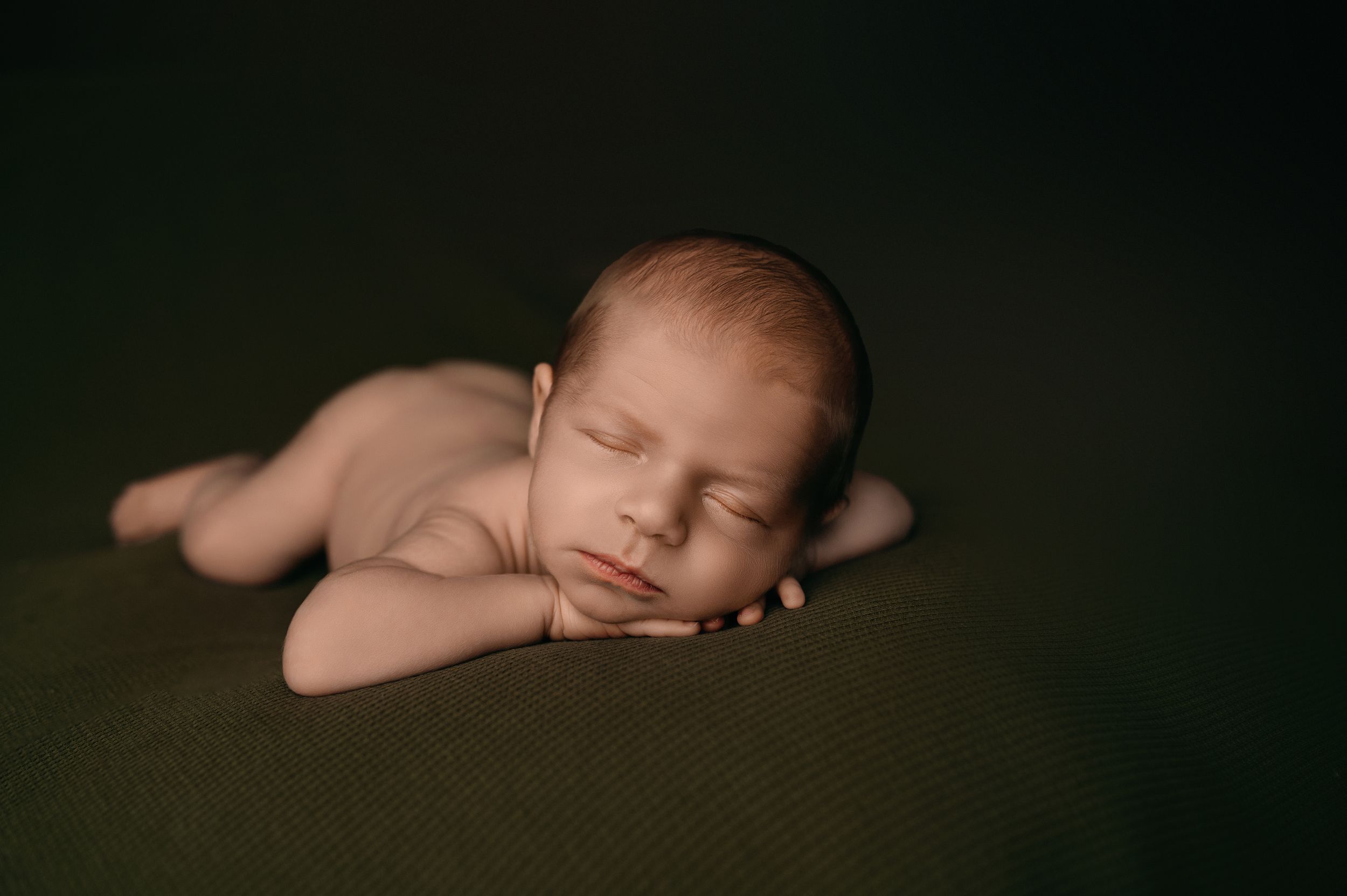 Peaceful newborn baby sleeping in dark blanket during professional photography session in studio.