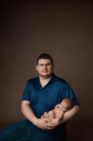 Four studio portraits of someone in a dark navy shirt holding a sleeping newborn baby against a brown backdrop.