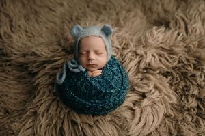 A series of artistic newborn photography portraits showing a sleeping baby wrapped in deep teal fabric on gray fur backdrop.