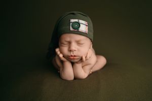 Sleeping baby gently nestled against soft brown backdrop with moody lighting.