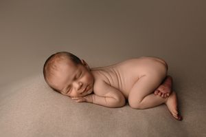 Closeup photo of sleeping newborn baby curled up in peaceful pose on beige backdrop.