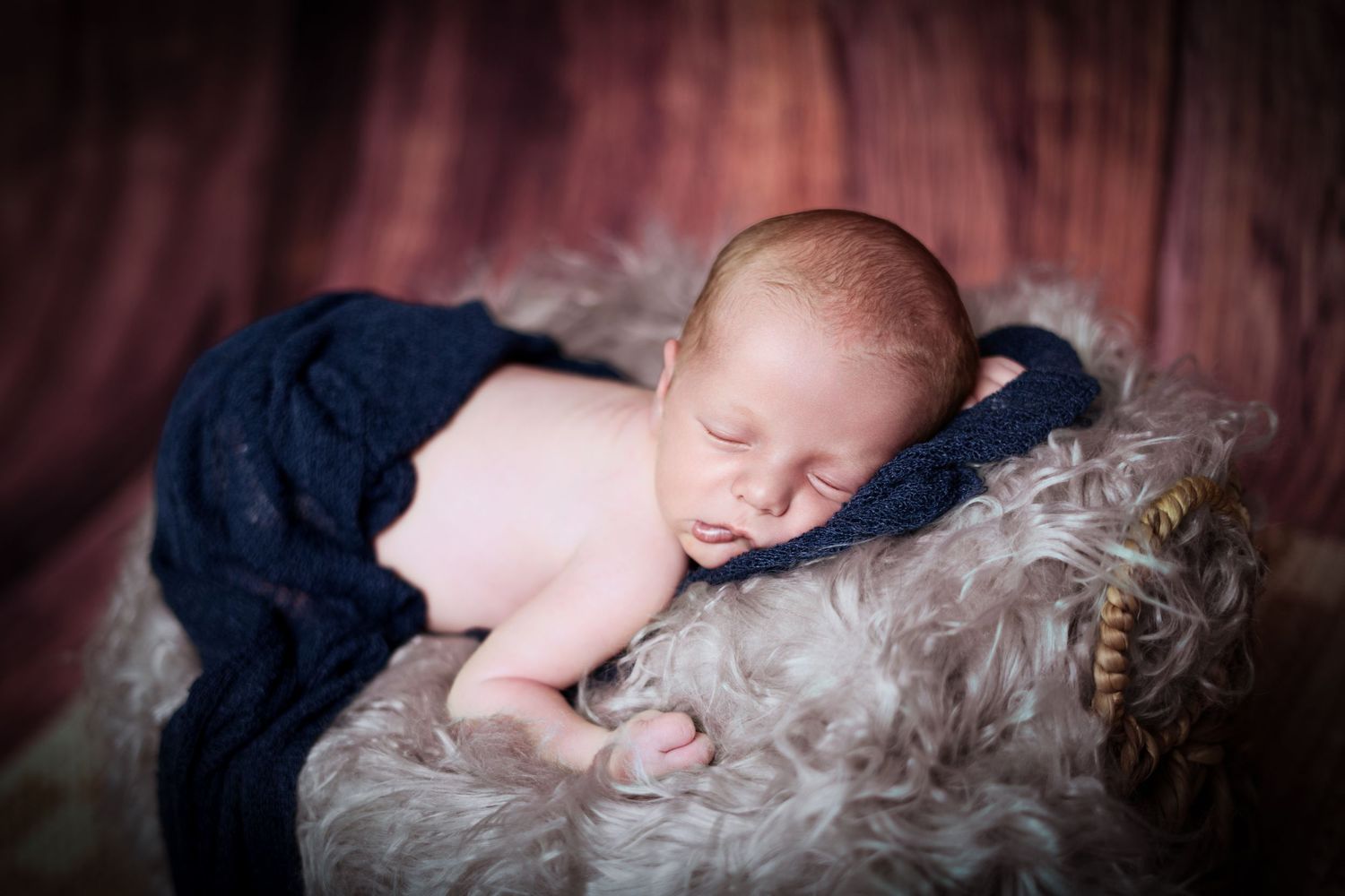 Artistic dark-toned newborn photography with soft textures and navy blue tones.
