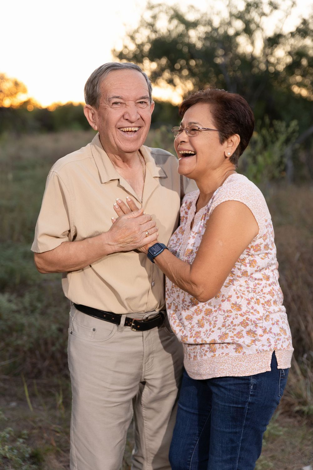 A couple embraces and laughs together in a natural outdoor setting during golden hour.