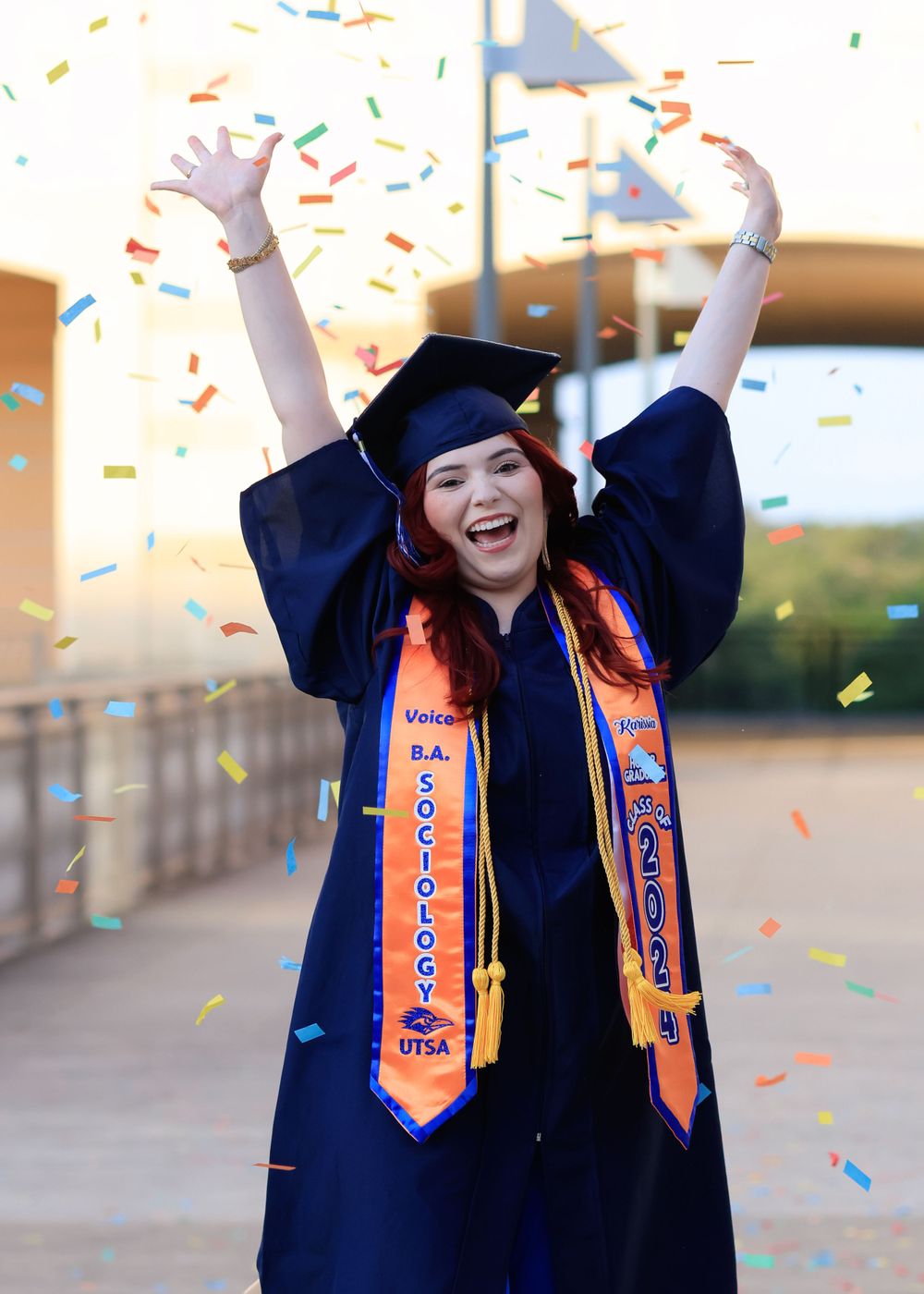 Graduate in blue cap and gown celebrates with confetti during graduation ceremony.