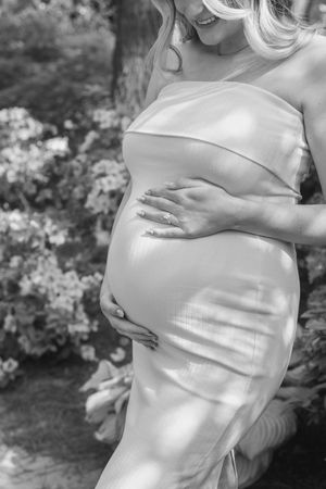 Black and white maternity photos showing a pregnant woman in an elegant dress.