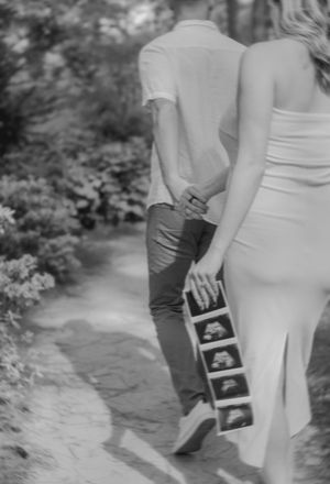 A couple holding ultrasound photos while walking outdoors.