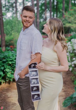 A couple shares a joyful moment while holding ultrasound photos in a garden setting.