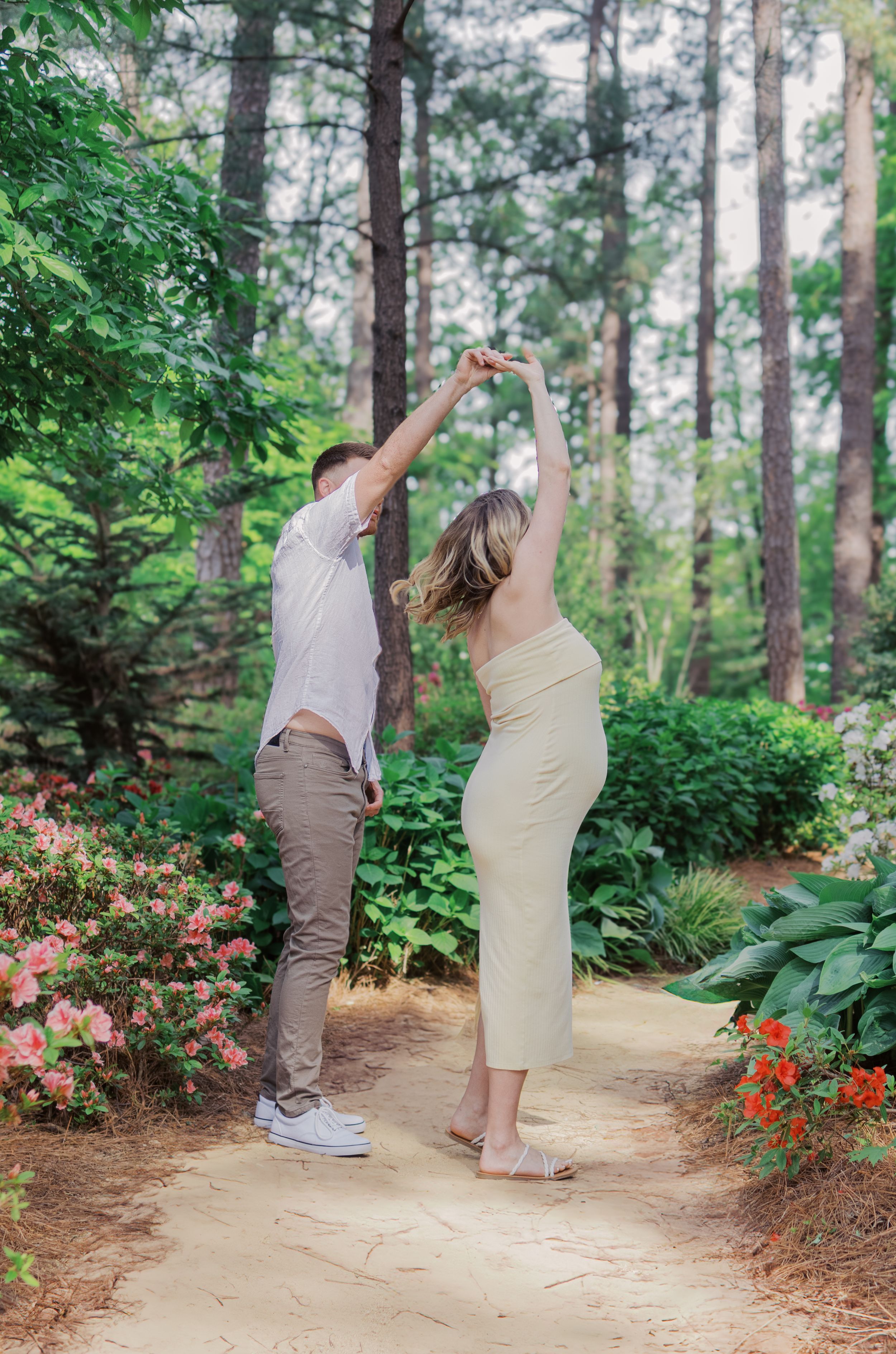 A couple dances together on a garden path surrounded by lush greenery and blooming flowers.