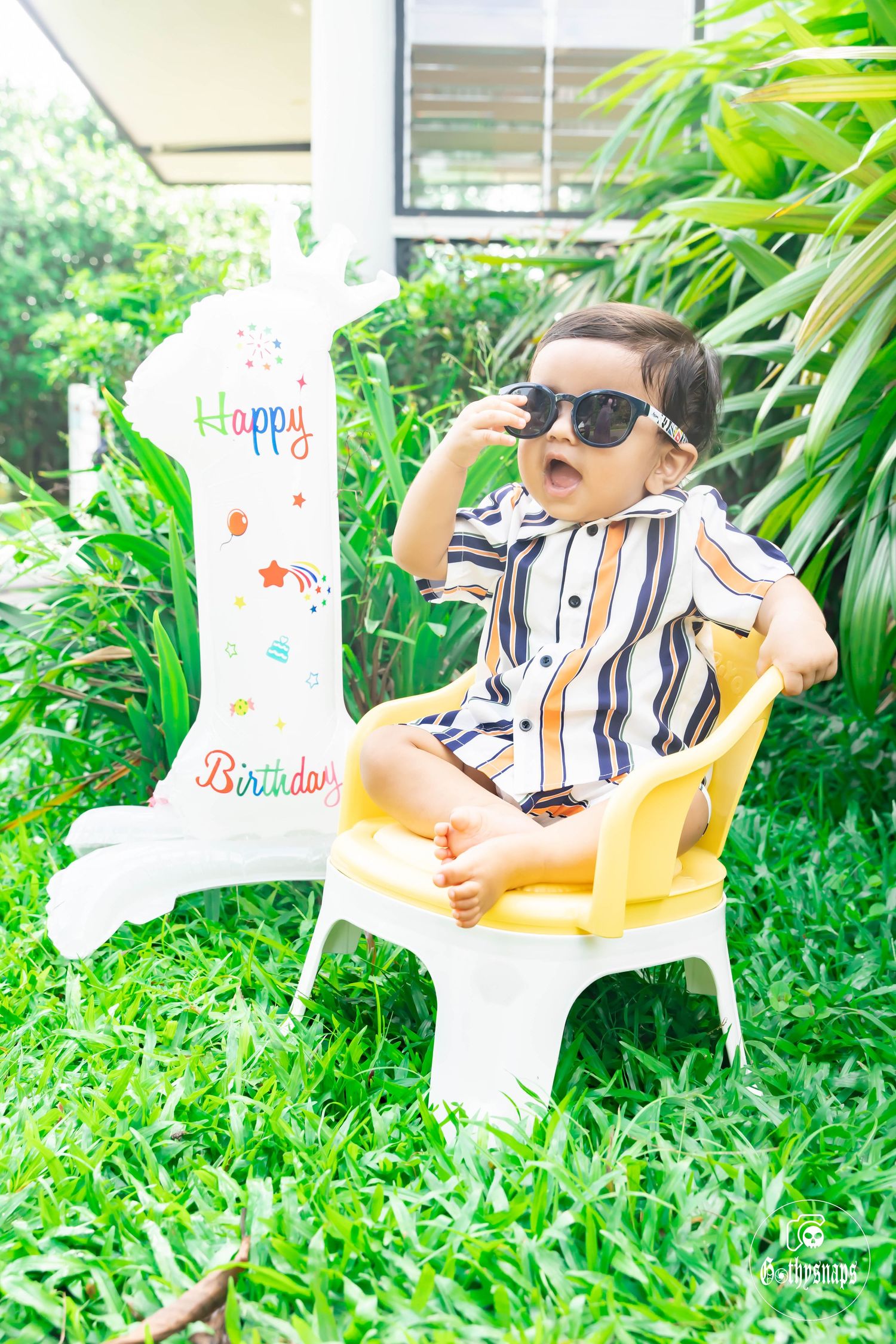 Infant in a white shirt sits in a yellow plastic chair outdoors on grass, showing various expressions and poses.