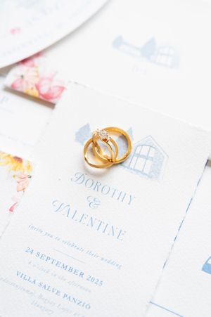Gold wedding rings resting on elegant Dorothy and Valentine wedding invitation card.