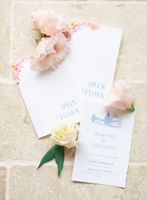 Elegant wedding vow books and invitation suite with pink flowers on stone surface.