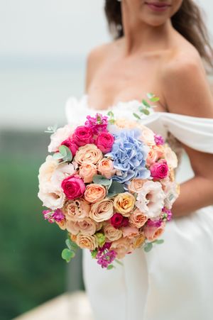 Close-up of a lush bridal bouquet with pink roses, hydrangeas, and peach blooms held by bride.