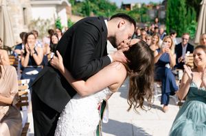 Newlyweds share passionate first kiss on dance floor while wedding guests applaud and celebrate.