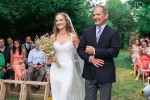 Bride walks down aisle with father in elegant lace wedding dress holding wildflower bouquet.
