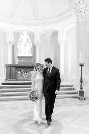 Bride and groom walk together in grand classical church interior in black and white photo.