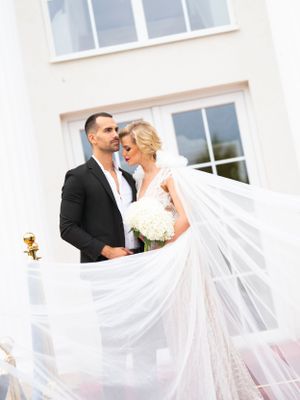 Elegant bride and groom embracing outdoors with wedding veil flowing dramatically in the foreground.
