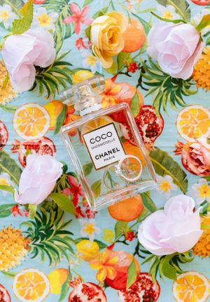 Coco Mademoiselle Chanel Paris perfume bottle surrounded by colorful roses and fruits on floral background.