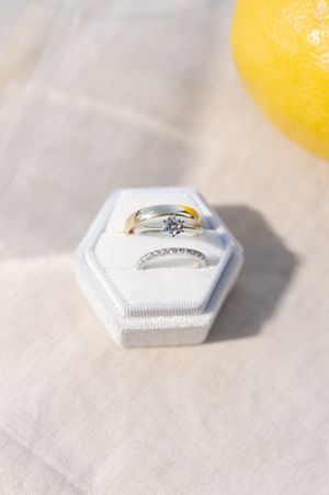 Diamond solitaire engagement ring and wedding band displayed in white hexagon velvet box.