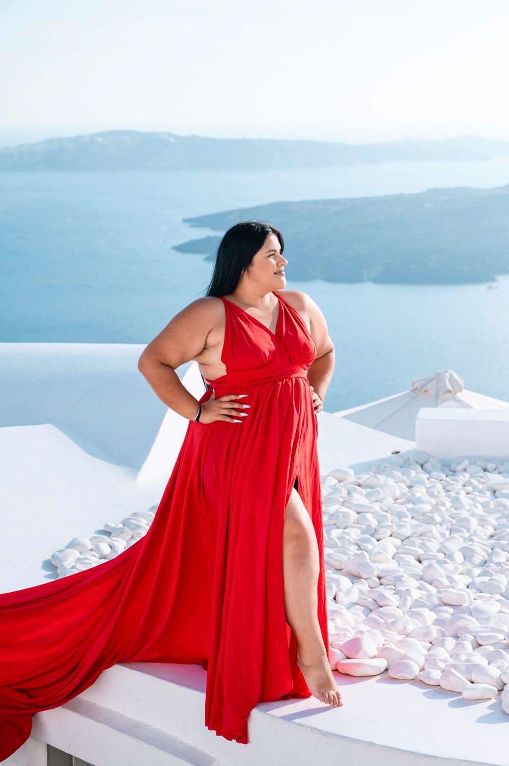 Woman in flowing red dress poses against white architecture and blue sea in Santorini.
