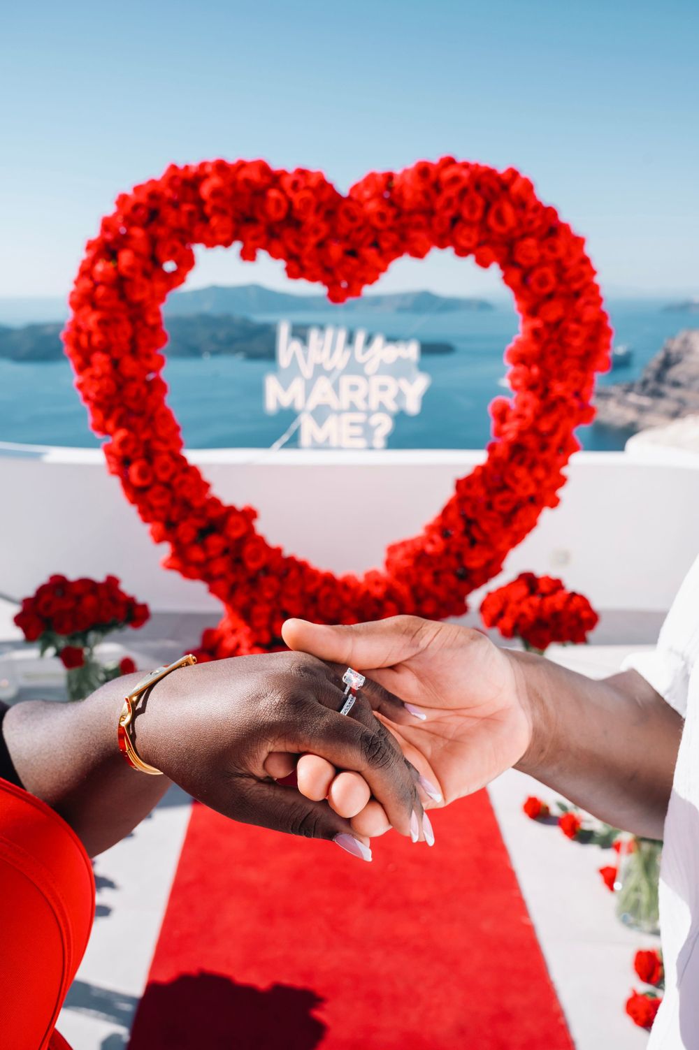 A red floral heart arch with 'Marry Me' text displayed against an ocean backdrop.