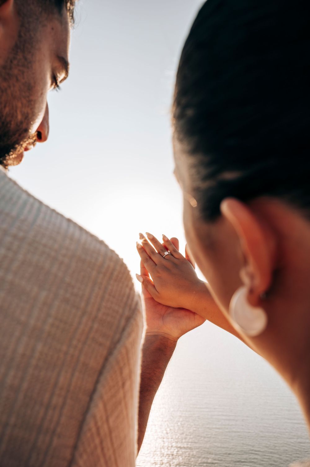 Close up shot of hands clasped during a romantic moment by the ocean.