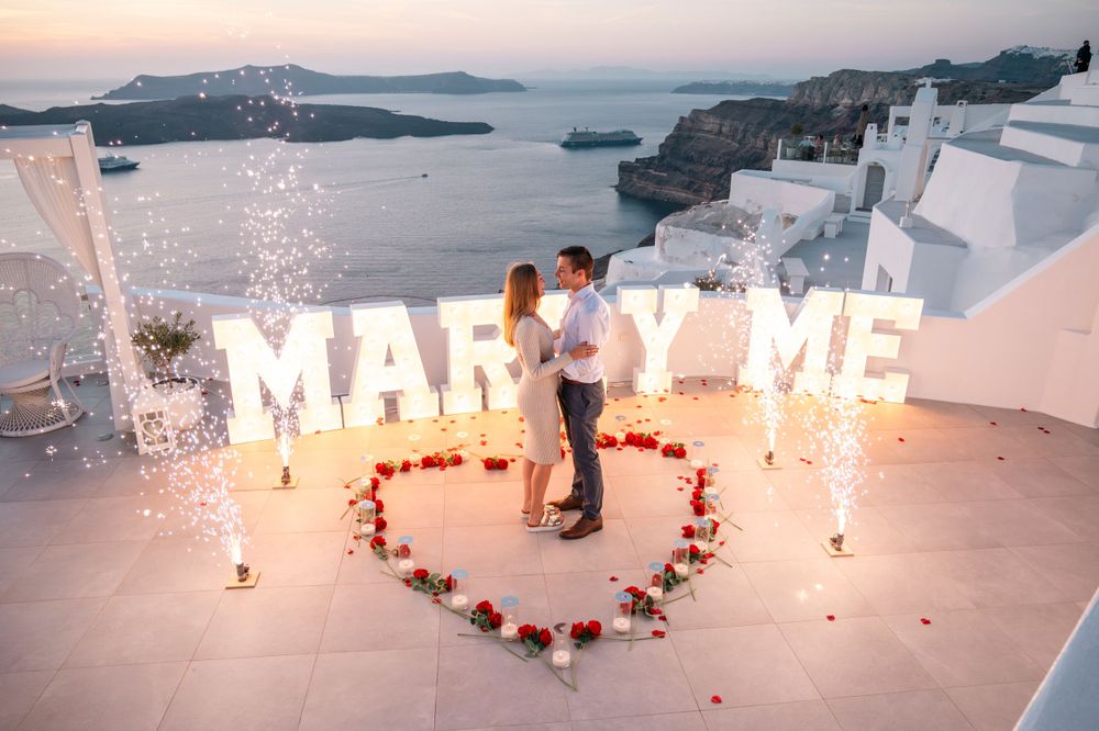 Romantic proposal setup with sparklers and 'Marry Me' sign on a rooftop overlooking the sea.
