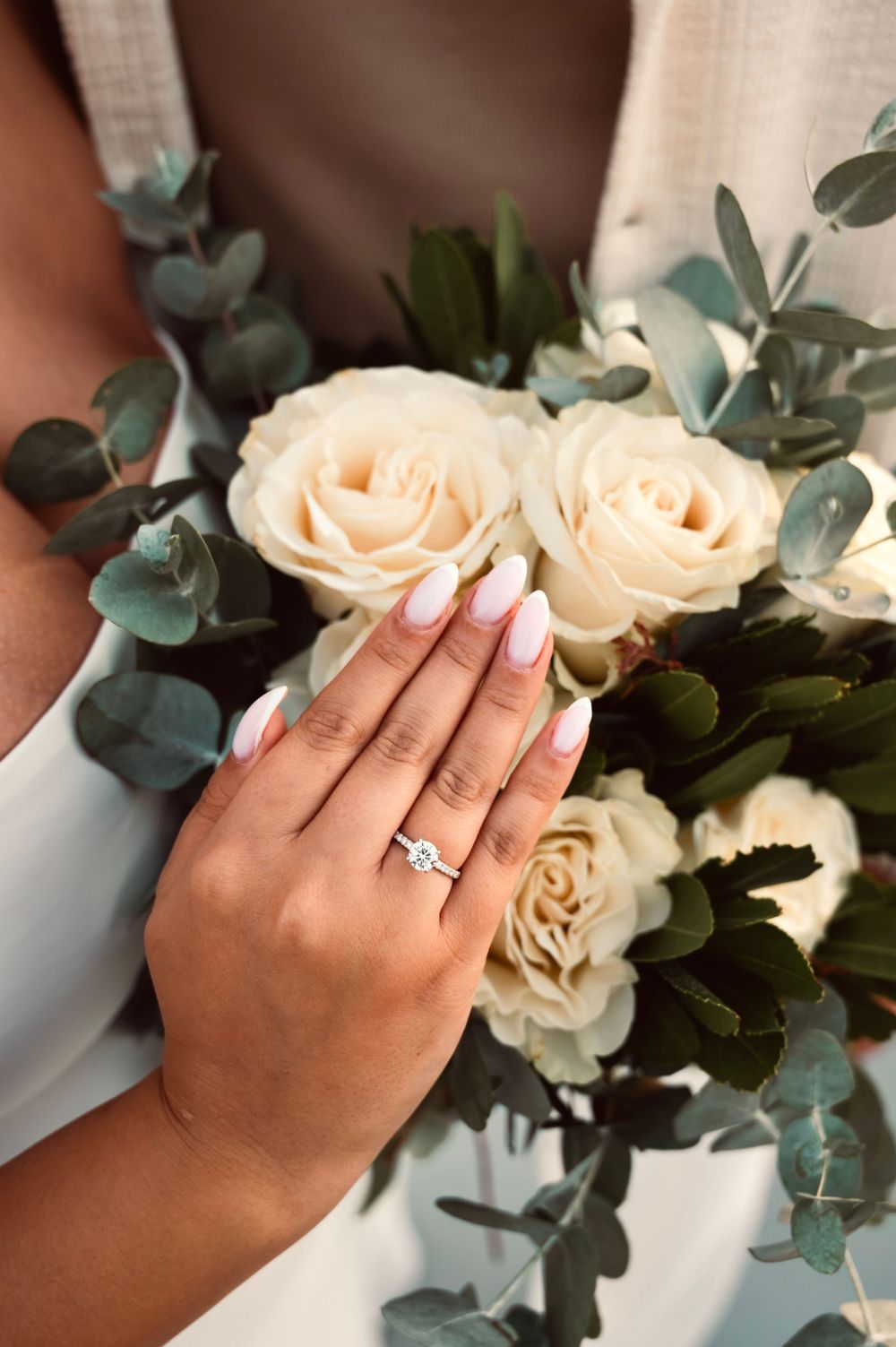 Elegant engagement ring displayed with cream roses and eucalyptus bouquet.