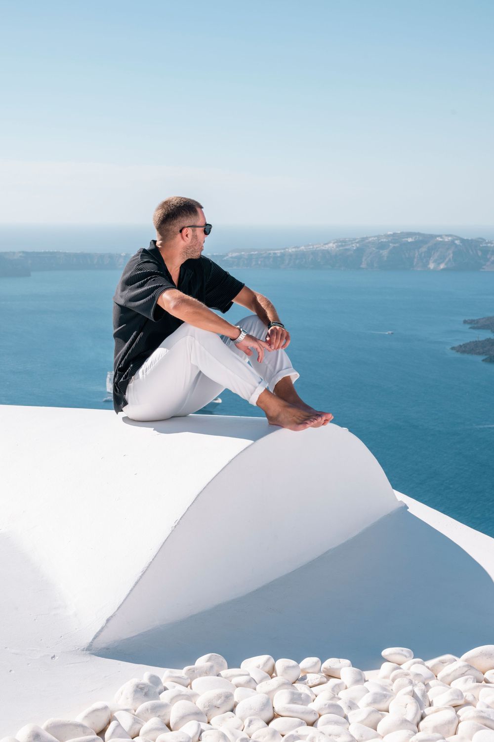 Person sitting on white rooftop wall overlooking Mediterranean Sea in Santorini.