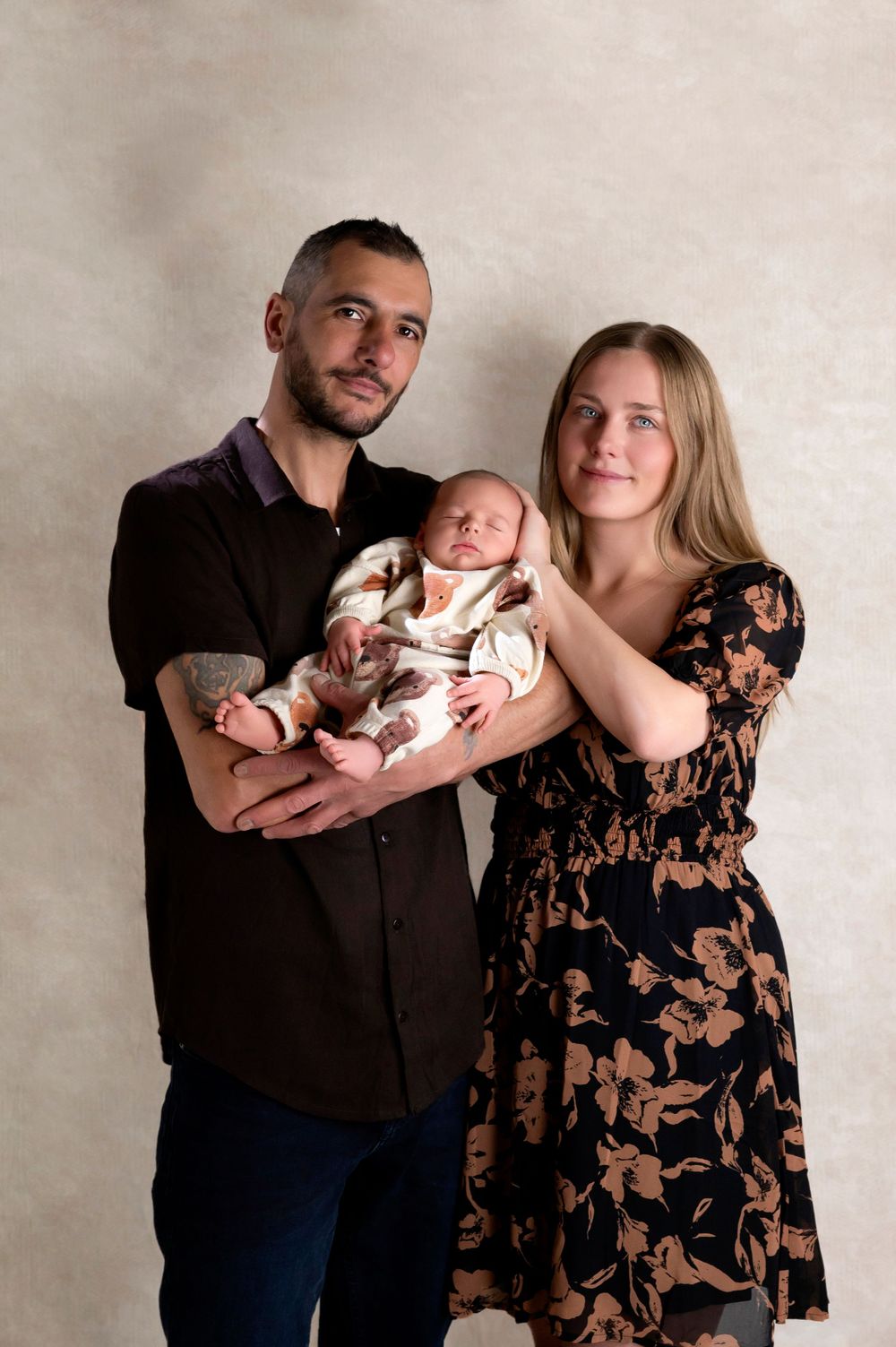 Family studio portrait in soft lighting with parents holding their newborn baby.