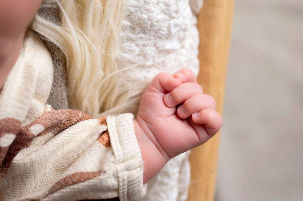 Close-up of tiny infant hand grasping white fabric in soft natural light.