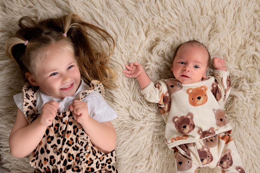 Two young children lying on a fluffy rug, one wearing leopard print and one in bear print clothing.