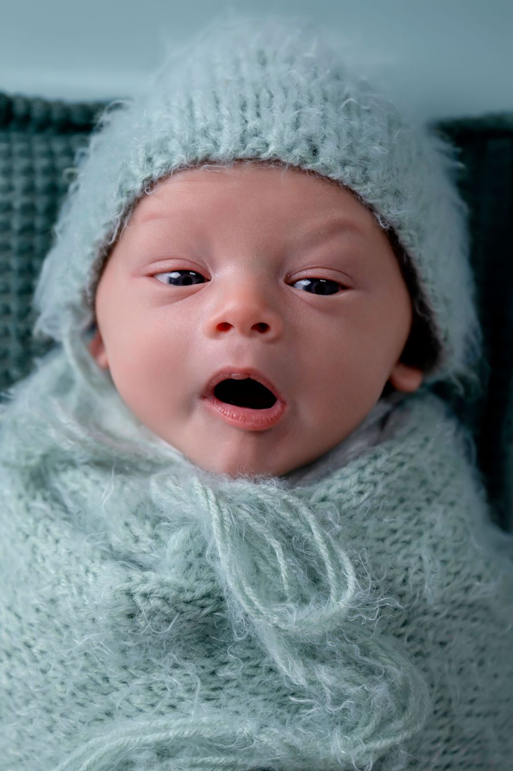 Alert baby wearing soft mint knit hat and wrap making expressive face.