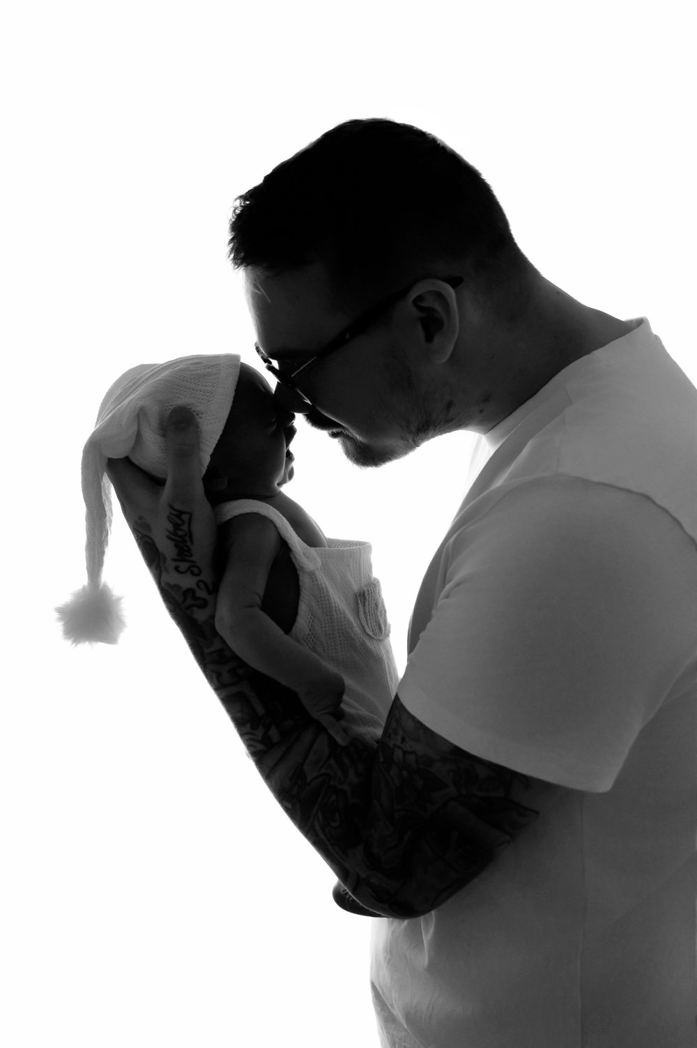 Silhouette profile of person in white shirt tenderly holding newborn with Santa hat.