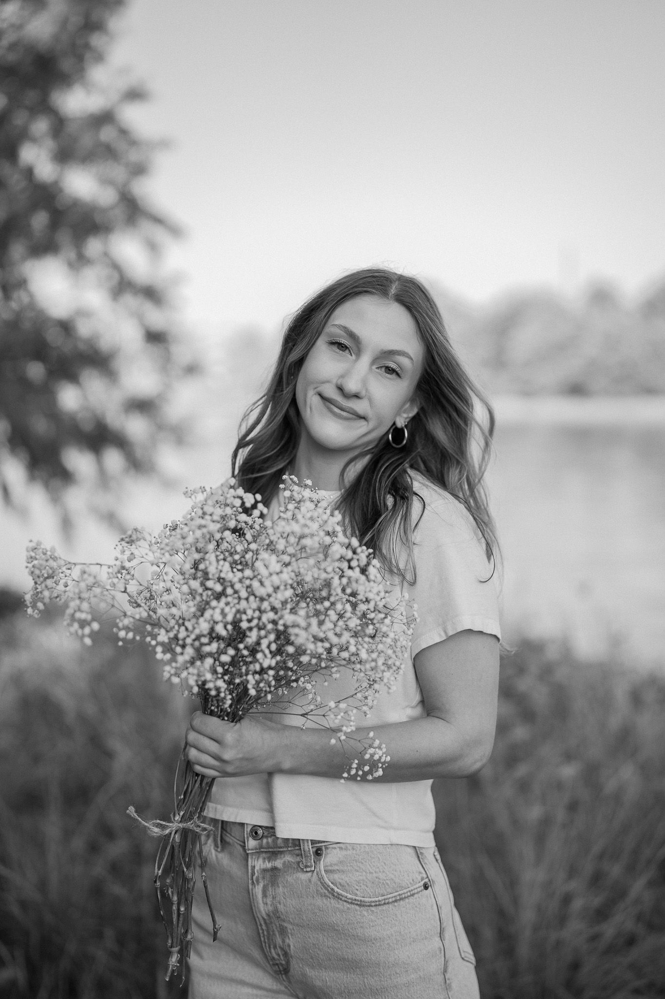 Black and white portrait with someone holding fresh baby's breath flowers by a serene lake.