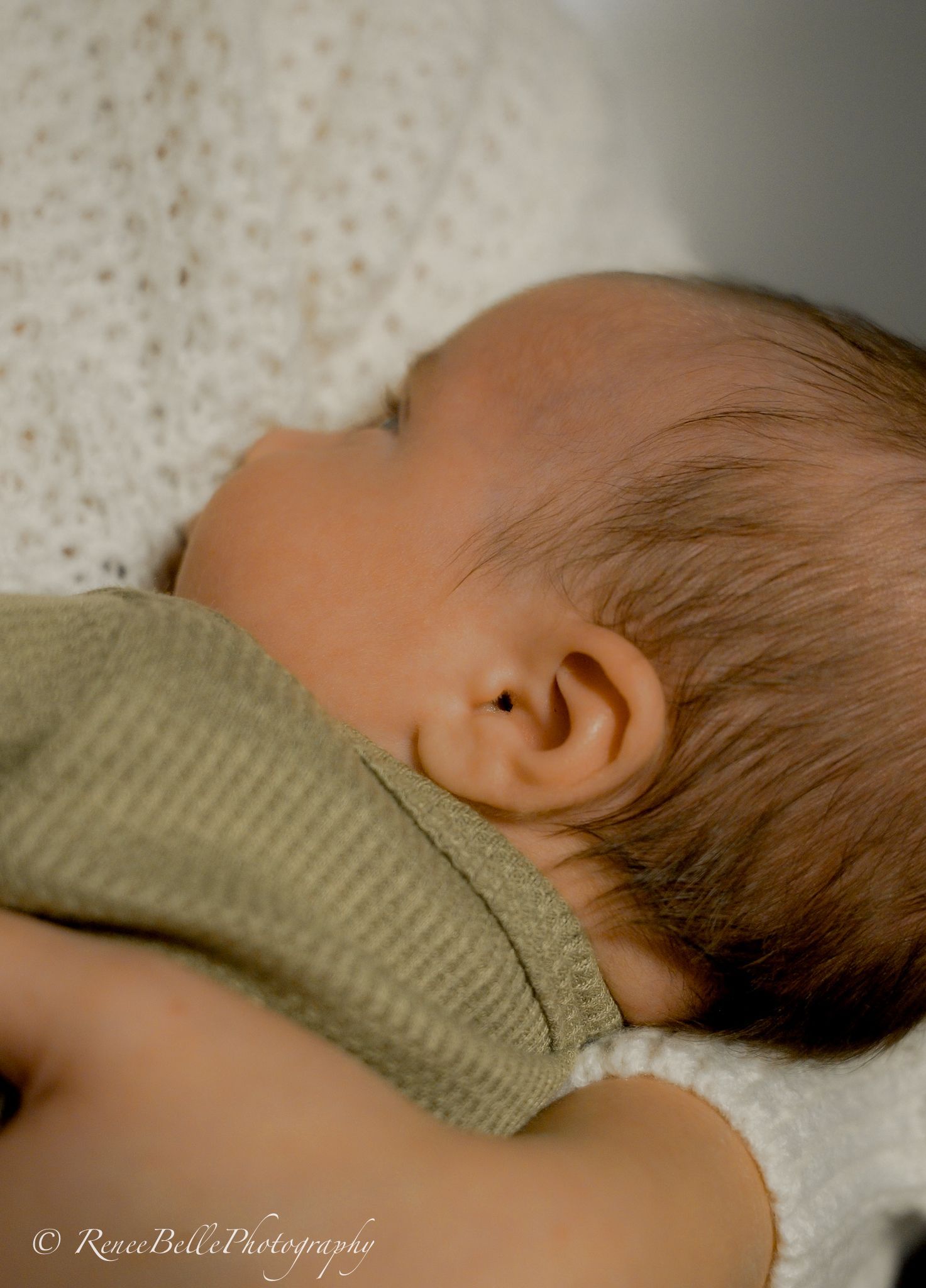 Close up of sleeping baby's ear and head against textured background.