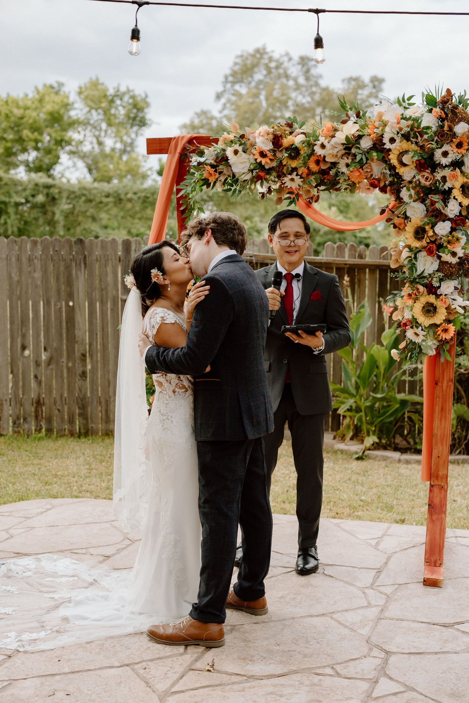 Outdoor wedding ceremony under a floral arch decorated with peach and cream blooms.